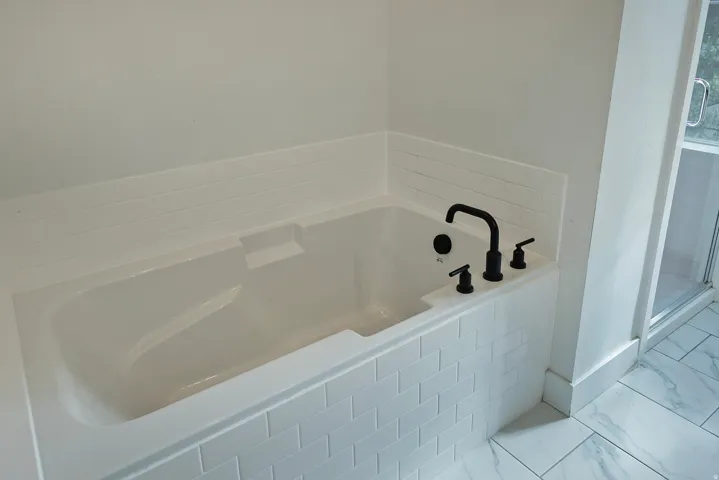 Built-in soaking tub with matte black fixtures, subway tile surround, and large format floor tiling