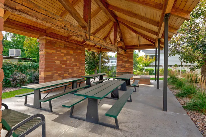 Covered outdoor gathering area featuring a wood-beam ceiling, stone-clad support walls, and a concrete paver base