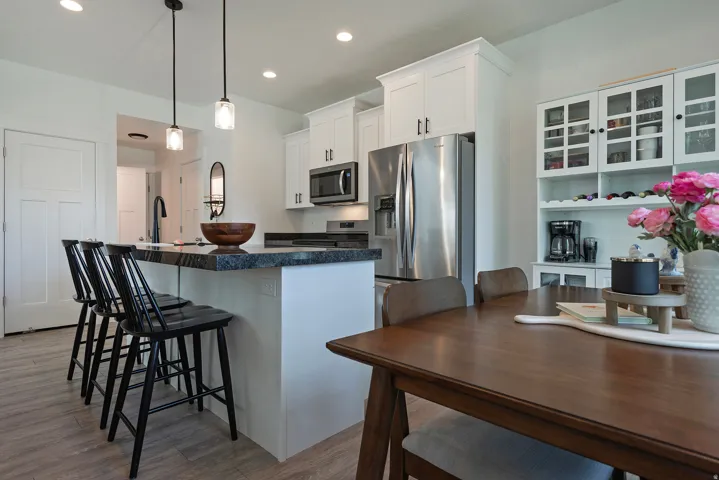 Kitchen featuring a breakfast bar with pendant lighting, white cabinetry, integrated stainless steel appliances, and wood-finish flooring