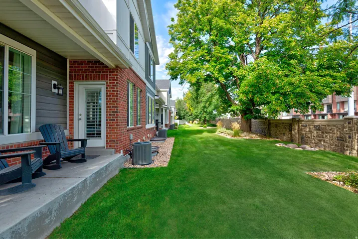 Private concrete patio with a white-framed glass door, red brick exterior, and lush green lawn