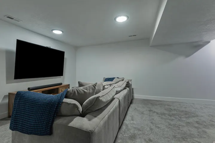Recessed ceiling lighting, wall-mounted television, wood-finish media console, and light gray wall paint