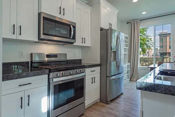 Stainless steel appliance package, white shaker-style cabinetry, dark speckled countertops, wood-finish flooring, and a built-in display cabinet