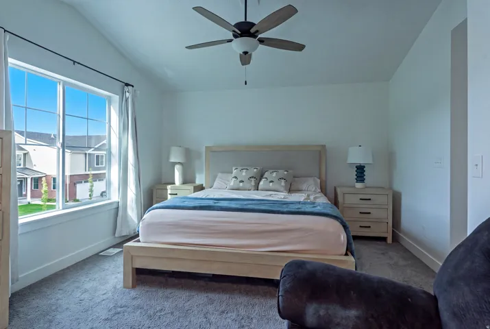 Vaulted ceiling with a ceiling fan, broad window, and plush carpeting