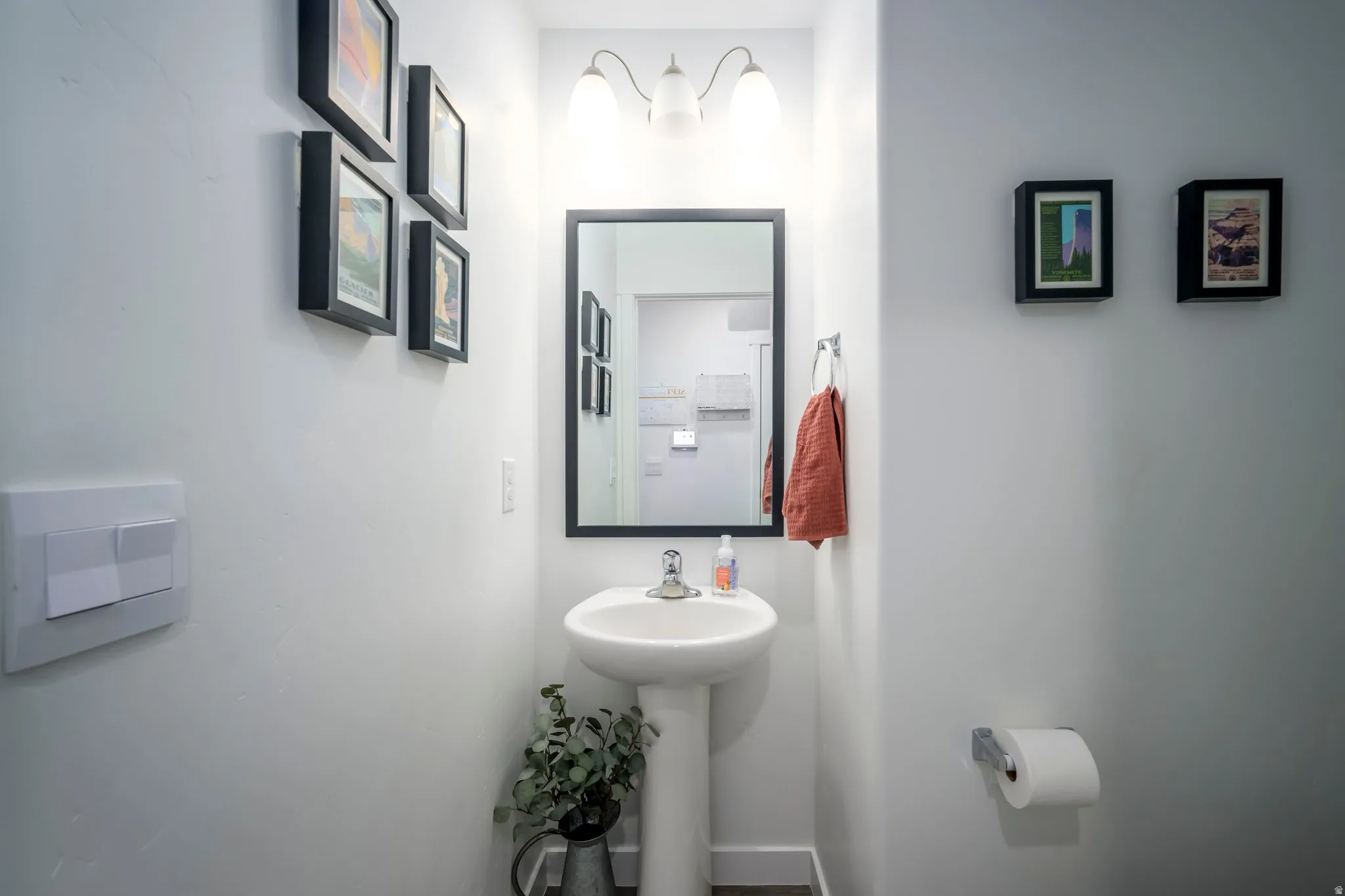 Pedestal sink with a wall-mounted mirror, brushed nickel towel ring, and overhead vanity lighting