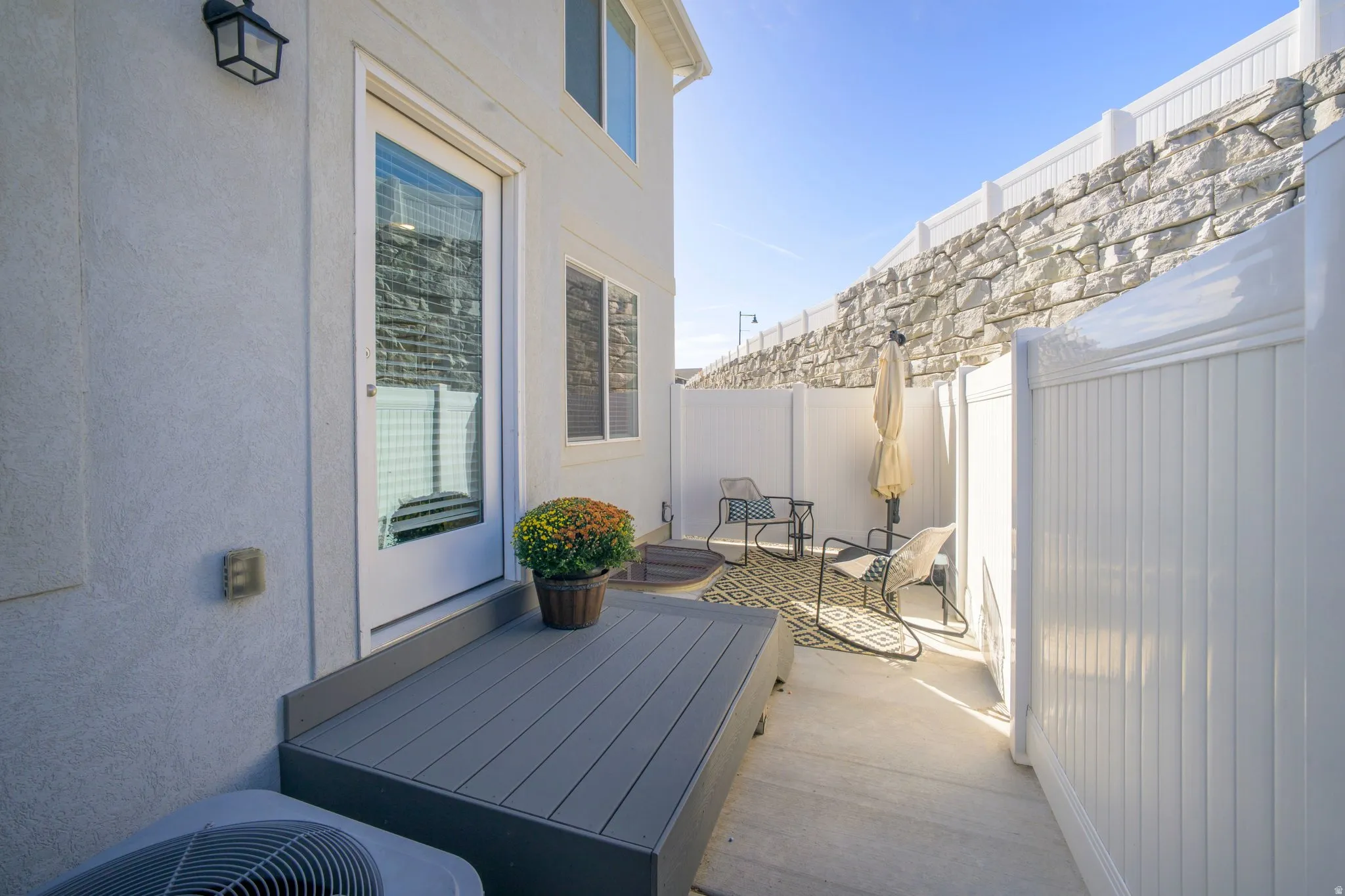 Private patio area featuring a composite deck, a full-lite exterior door, and white privacy fencing