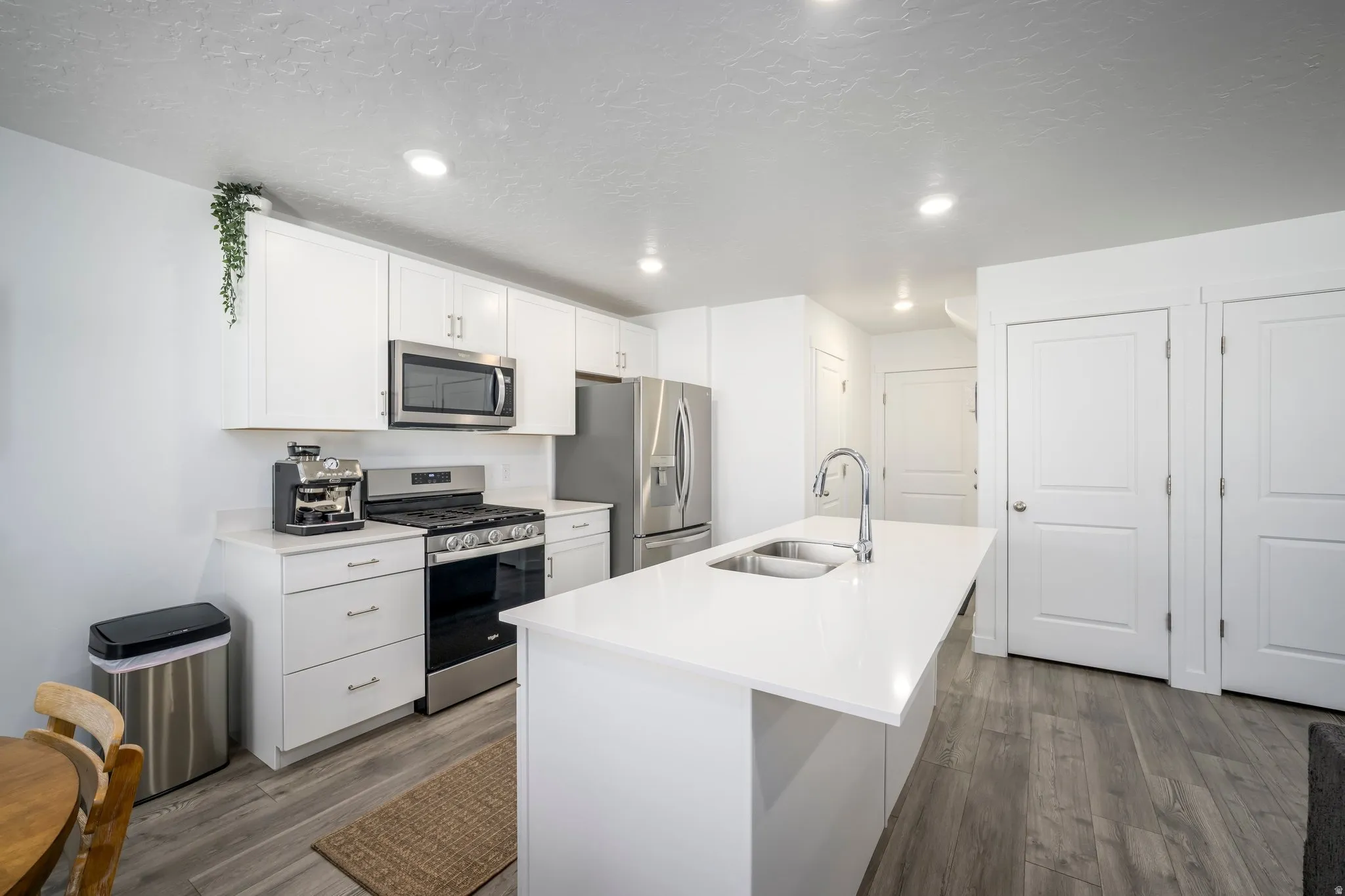 Modern kitchen featuring white cabinetry, stainless steel appliances, a center island with an undermount sink, and wood-finish flooring