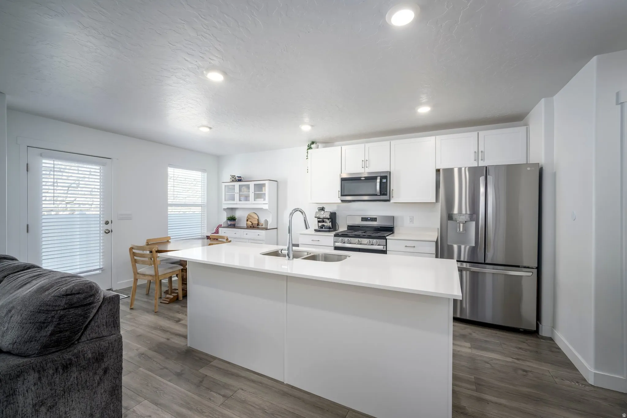 Kitchen featuring a large island with sink, white shaker cabinetry, stainless steel appliances, and wood-finish flooring
