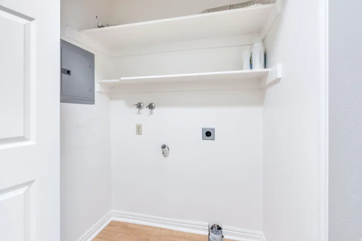 Laundry area featuring wood-finish flooring, two wall-mounted shelves, and an electrical panel
