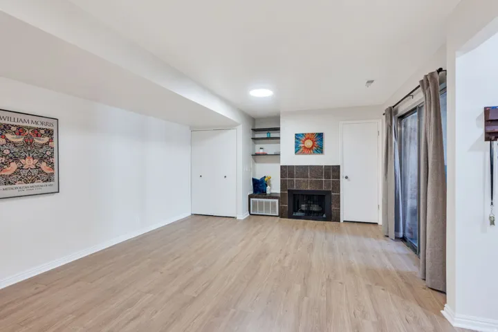 Wood-finish flooring, built-in shelving, tile-surround fireplace, sliding glass door, and recessed lighting