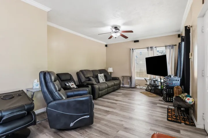 Living room featuring wood-finish flooring, a ceiling fan with light fixture, and crown molding