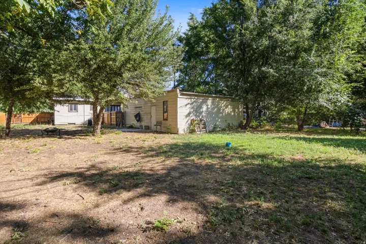 Expansive yard with mature trees, detached structure, concrete patio, and fenced perimeter