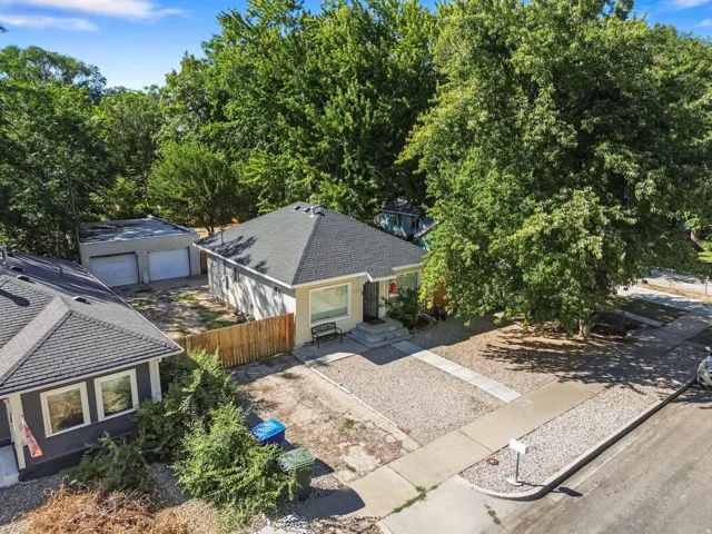 Single-story residence with a dark shingled roof, stucco exterior, and mature trees
