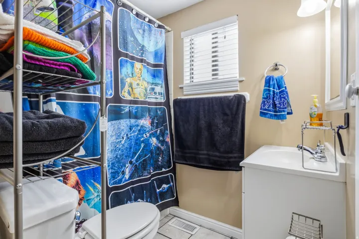 White vanity with integrated sink, chrome faucet, wall-mounted mirror, and horizontal window blinds