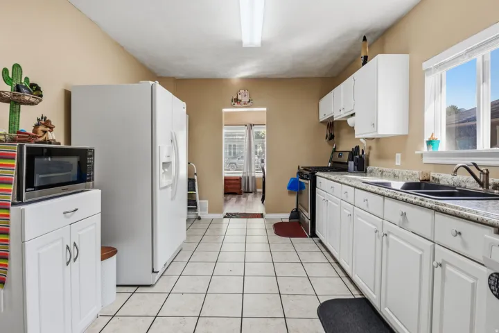 Kitchen featuring white cabinetry, light-toned tile flooring, dual-basin sink with a bronze-finish faucet, and a window