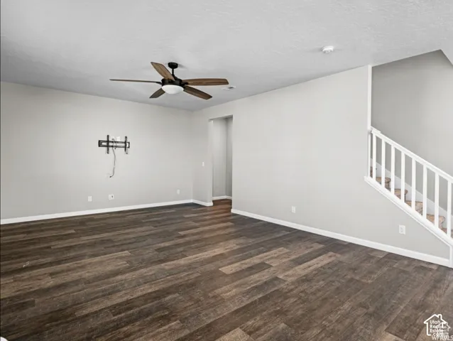Wood-finish flooring, staircase with white railing, ceiling fan with integrated lighting, and neutral wall tones