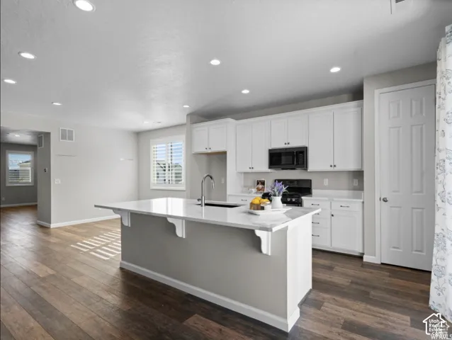 Spacious kitchen featuring an island with a light-toned countertop, white cabinetry, integrated black appliances, recessed lighting, and wood-finish flooring