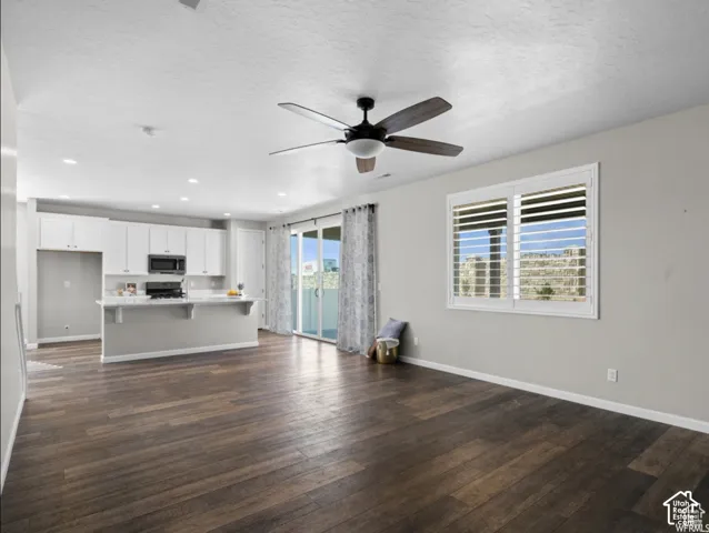 Open-concept living space featuring wood-finish flooring, a contemporary ceiling fan, white shaker cabinetry, a kitchen island with seating, and a glass sliding door