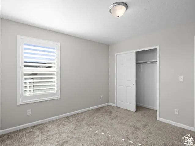 Carpeted room featuring a window with plantation shutters, a sliding bi-fold closet, and a semi-flush mount ceiling light fixture
