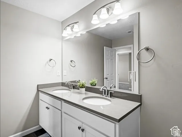 Double vanity with integrated sinks, gray countertop, white cabinetry, and wall-mounted vanity lighting
