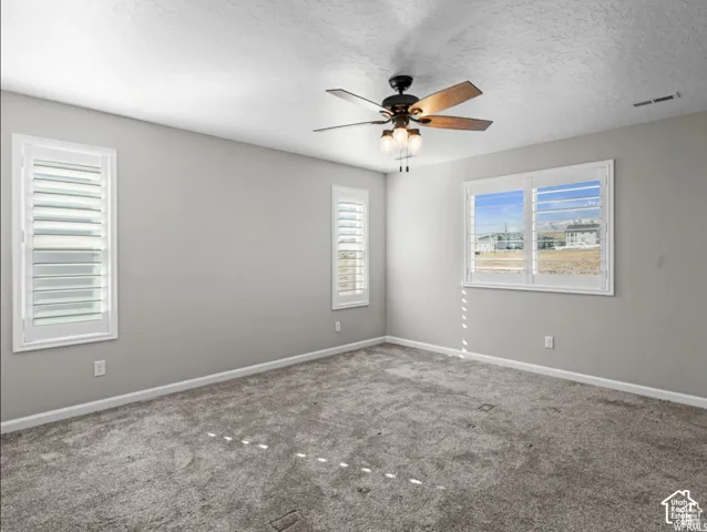 Neutral wall paint, textured ceiling, ceiling fan with integrated lighting, window with white louvered shutters, carpeted flooring