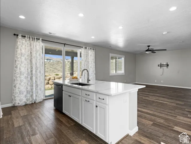 Kitchen island with a white countertop and integrated sink, stainless steel faucet, white cabinetry with dark hardware, and a built-in dishwasher