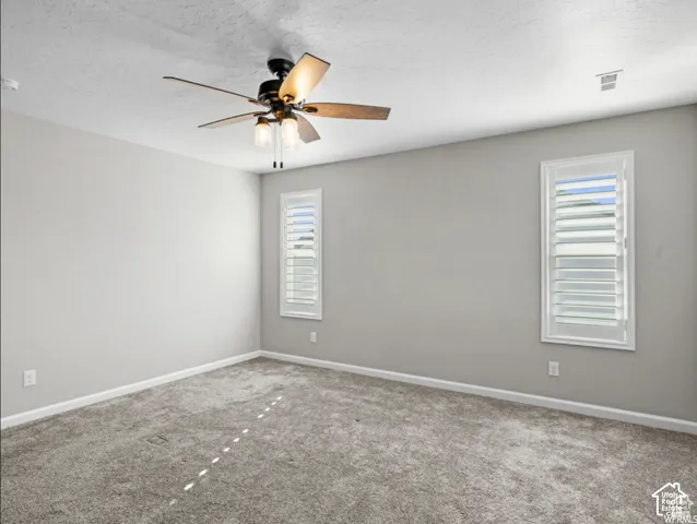 Wall-to-wall carpeting, two windows with louvered shutters, and a ceiling fan with integrated lighting