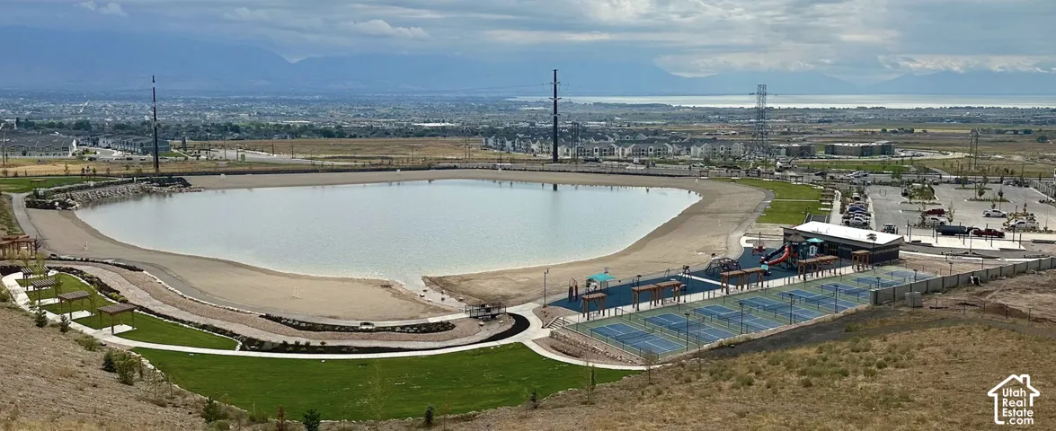 Expansive community lake with sandy beach areas, adjacent recreational courts, a dedicated play area, and a large parking facility