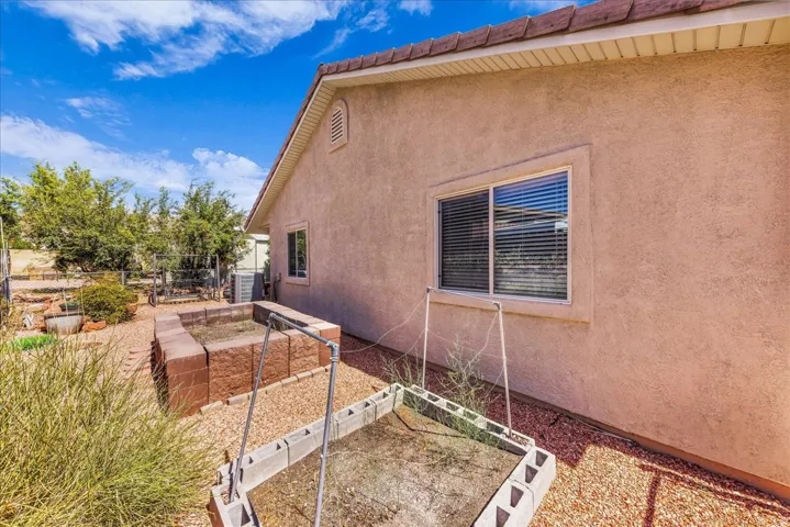 Stucco exterior with a tiled roofline, featuring a dual-pane window, gravel landscaping, and raised garden beds