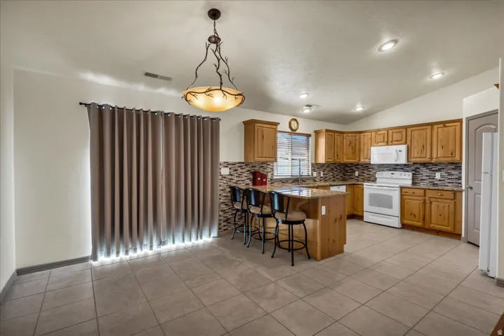 Kitchen with wood cabinetry, tile backsplash, and an island with bar seating