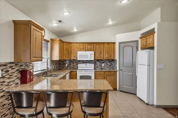 Kitchen featuring wood cabinetry, granite countertops, tile backsplash, stainless steel sink, and recessed lighting