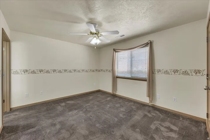 Neutral wall paint with decorative border, window with blinds, ceiling fan, and carpeted flooring