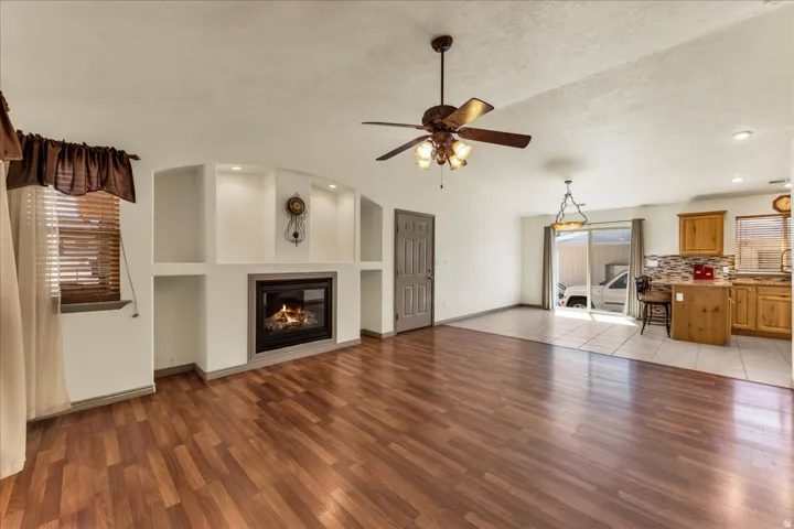 Built-in fireplace with display shelving, wood-finish flooring, ceiling fan, kitchen island with seating, and sliding glass door