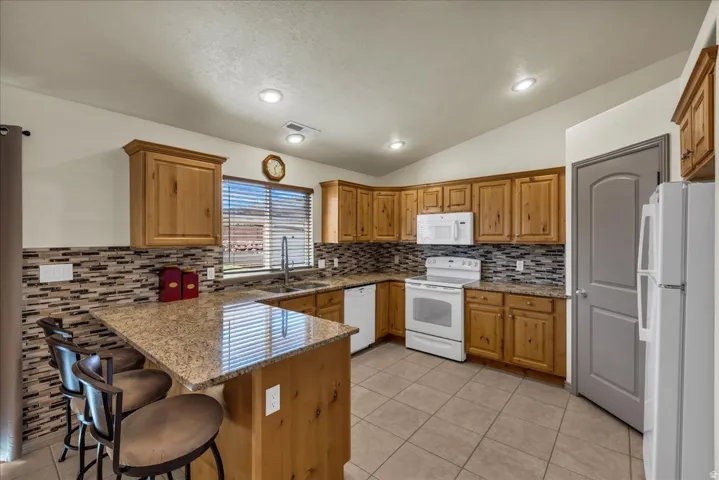 Kitchen featuring wood cabinetry, granite-style countertops, mosaic tile backsplash, and tile flooring