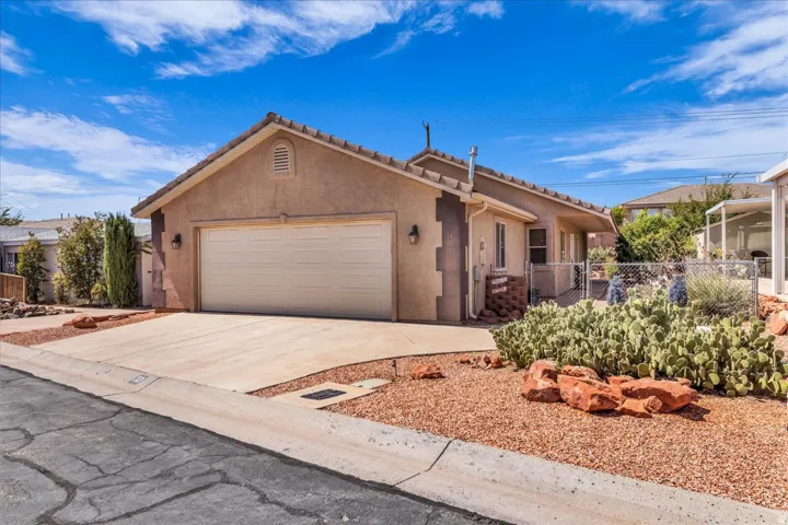 Stucco exterior with a two-car garage, concrete driveway, and a low-maintenance desert landscape featuring cacti and decorative rocks