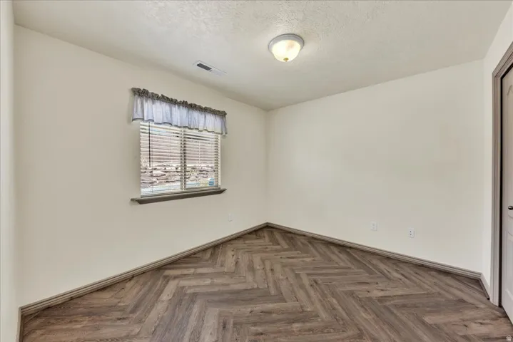 Room featuring wood-finish flooring in a herringbone pattern, a single window with blinds, and recessed lighting