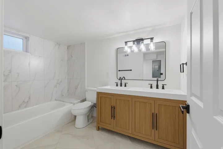 Double vanity with dual sinks, warm wood-finish cabinetry, and matte black fixtures