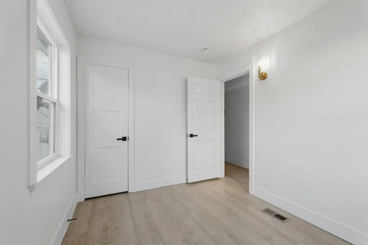 Wood-finish flooring, white paneled doors with matte black hardware, and a brass wall sconce