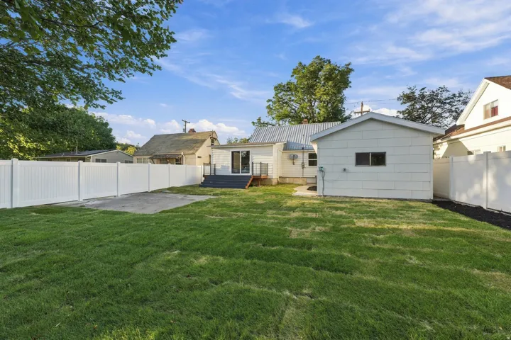 Expansive green lawn, white privacy fencing, rear deck with dark flooring, detached outbuilding, and sliding glass door access