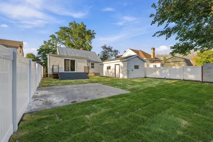 Expansive backyard featuring a manicured lawn, concrete patio, and a detached building