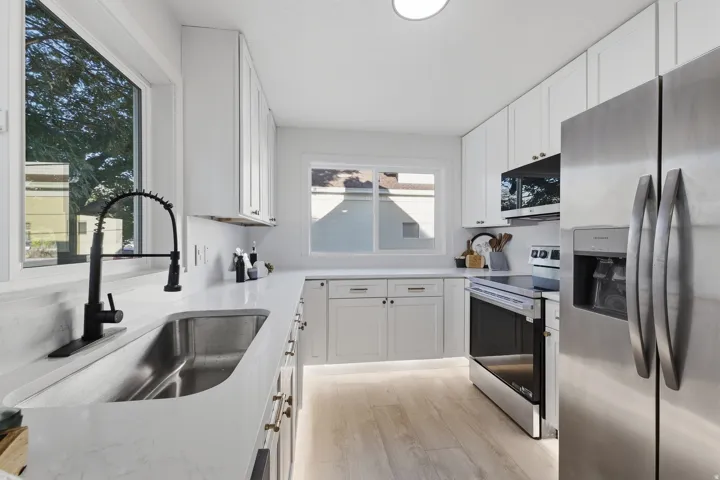 Stainless steel appliances, white cabinetry, undermount sink, black pull-down faucet, and wood-finish flooring