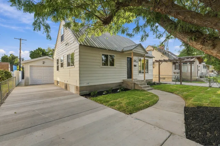 Exterior featuring white siding, a metal roof, covered entry, and a concrete driveway leading to a detached garage
