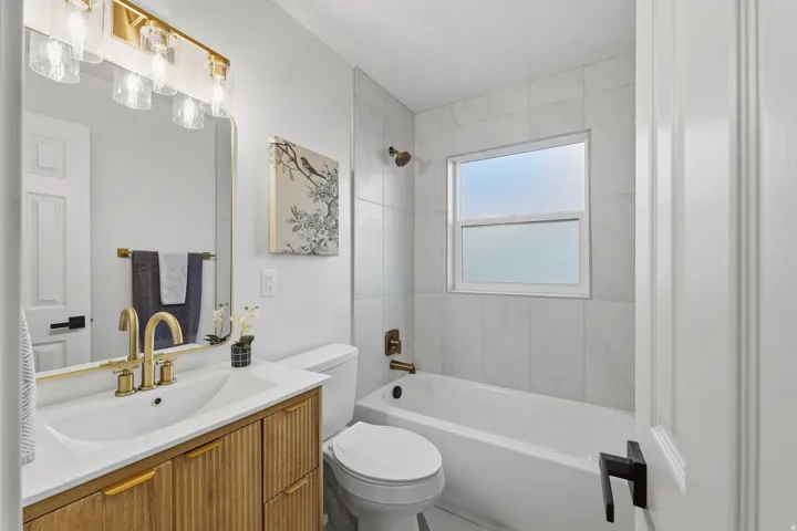 Bathroom featuring a wood-finish vanity with a white countertop, gold-tone fixtures, a built-in bathtub with a tile surround, and a window