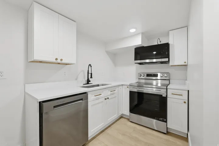White cabinetry, stainless steel appliances, wood-finish flooring, white countertops, and a matte black faucet