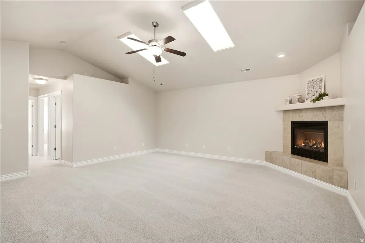 Vaulted ceilings with multiple skylights, recessed lighting, ceiling fan, and a tiled fireplace