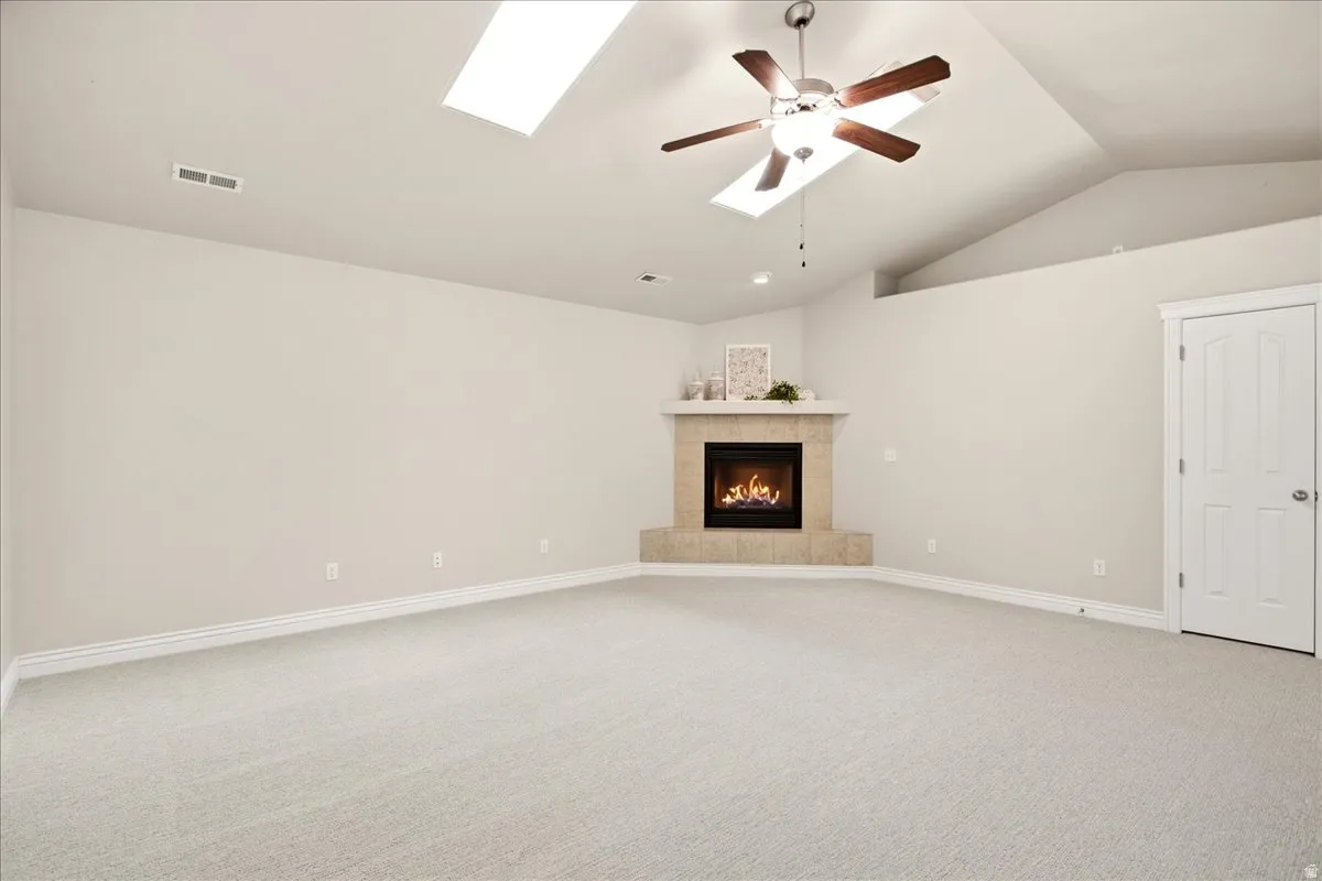 Vaulted ceiling with skylights and ceiling fan, corner fireplace with tile surround, and carpet flooring