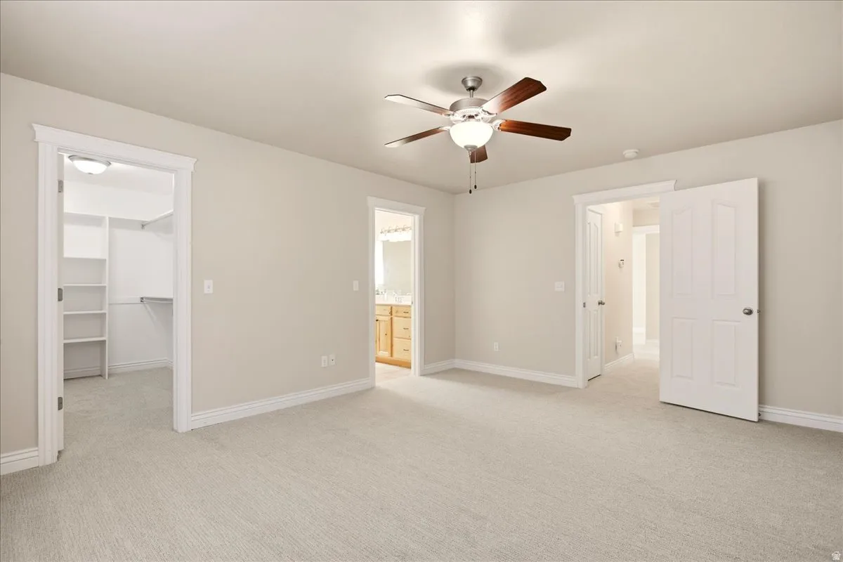 Expansive carpeted room featuring a ceiling fan with light fixture, walk-in closet with built-in shelving