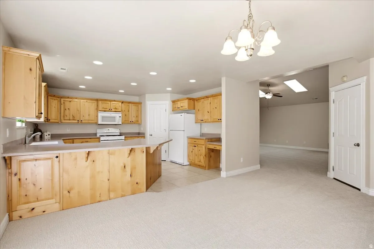 Kitchen featuring light wood cabinetry, white appliances, and a peninsula with countertop seating