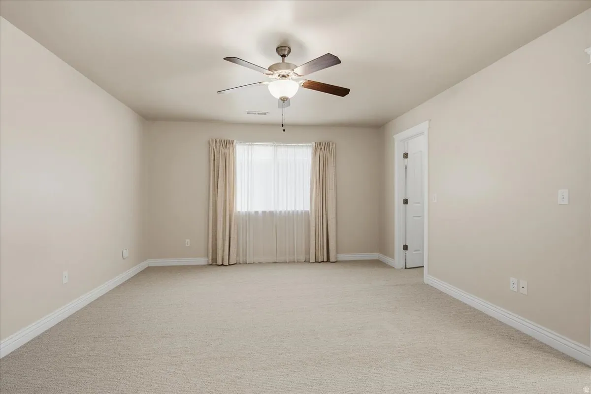 Primary bedroom featuring a ceiling fan with integrated lighting, a window with sheer and solid curtains, and light-toned walls
