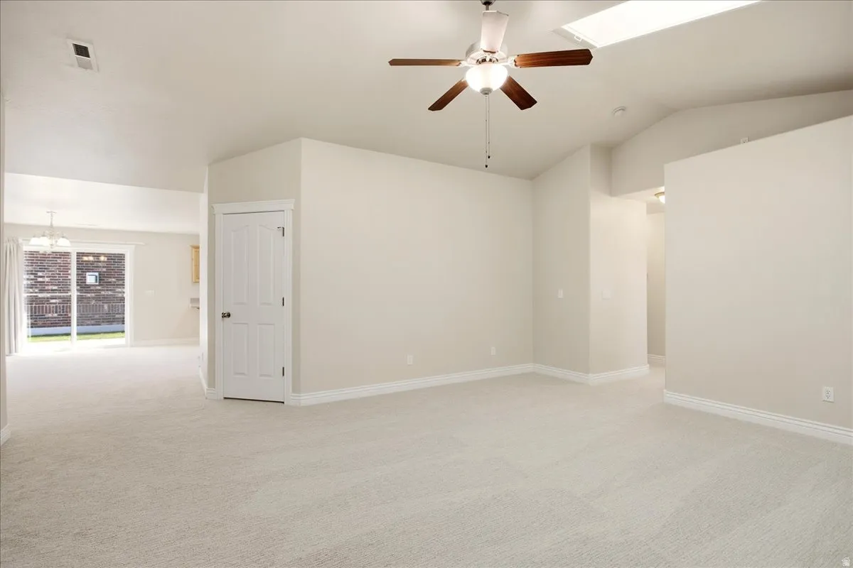 Vaulted ceilings with a skylight, ceiling fan, and light-toned carpeting throughout