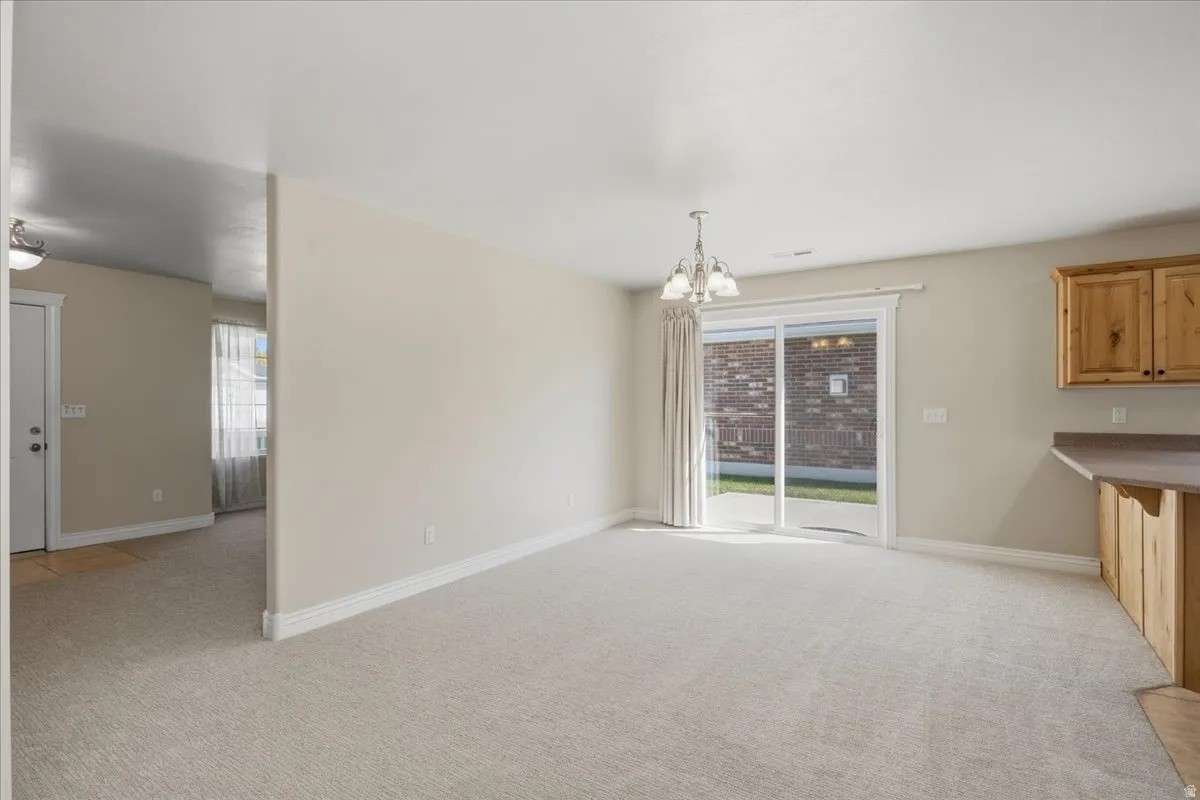 Carpeted living area with a sliding glass door, overhead chandelier, light wood cabinetry